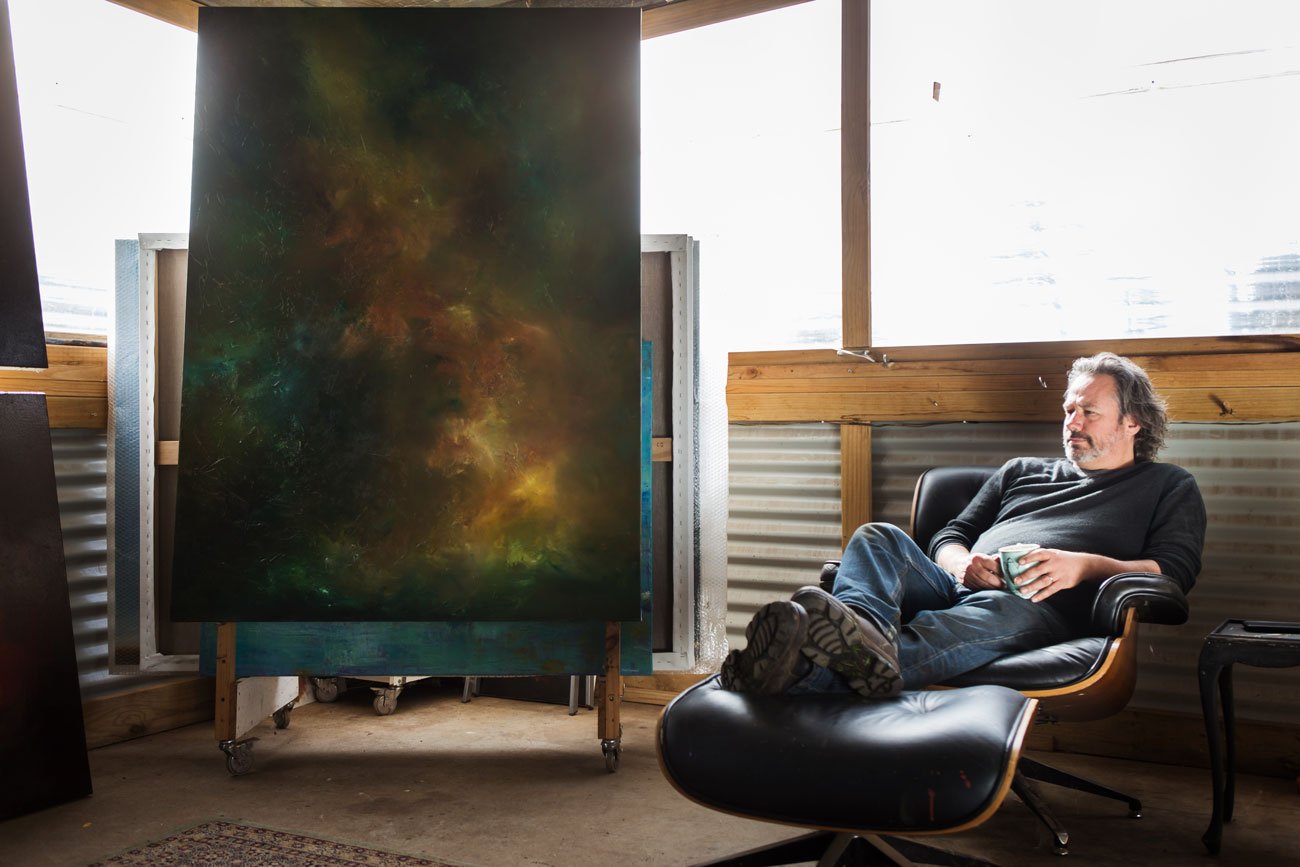 Artist lounging in chair next to painting
