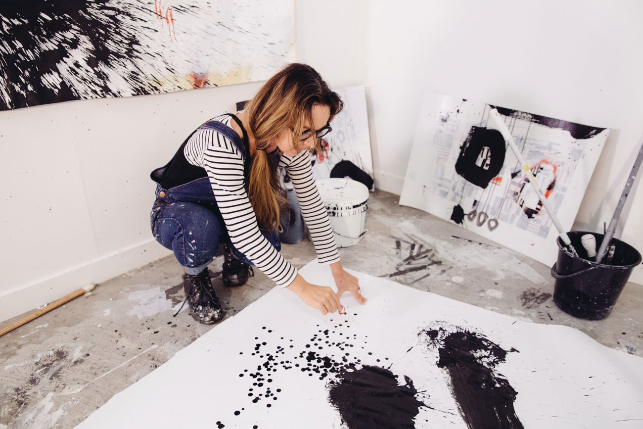 artist adding red pastel to large painting on the floor of her studio