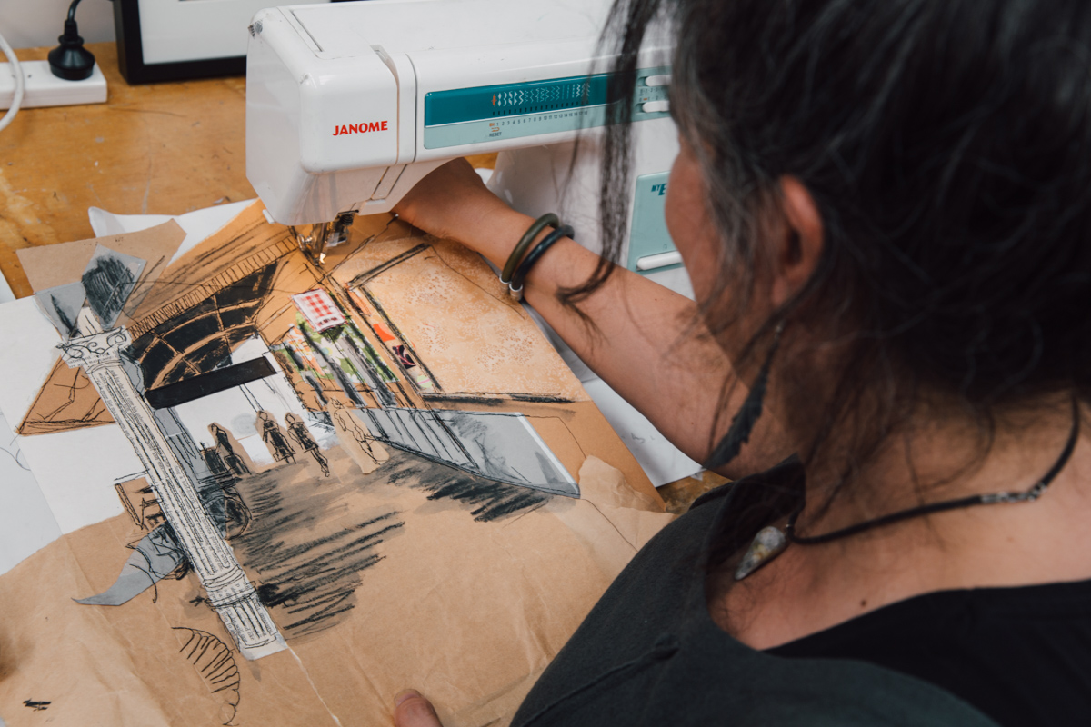 artist using sewing machine to sketch on brown paper