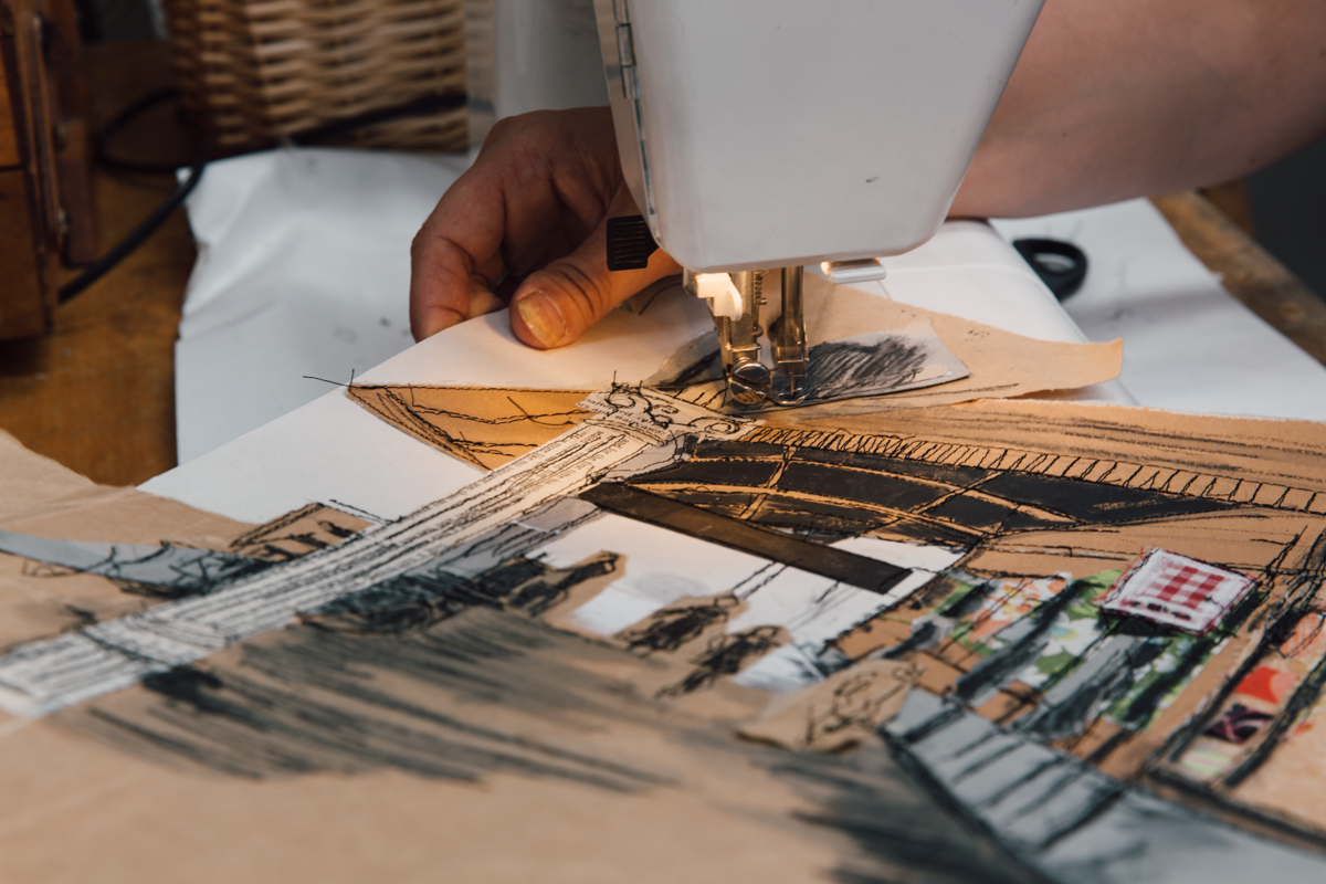 artist using sewing machine to embroider brown paper