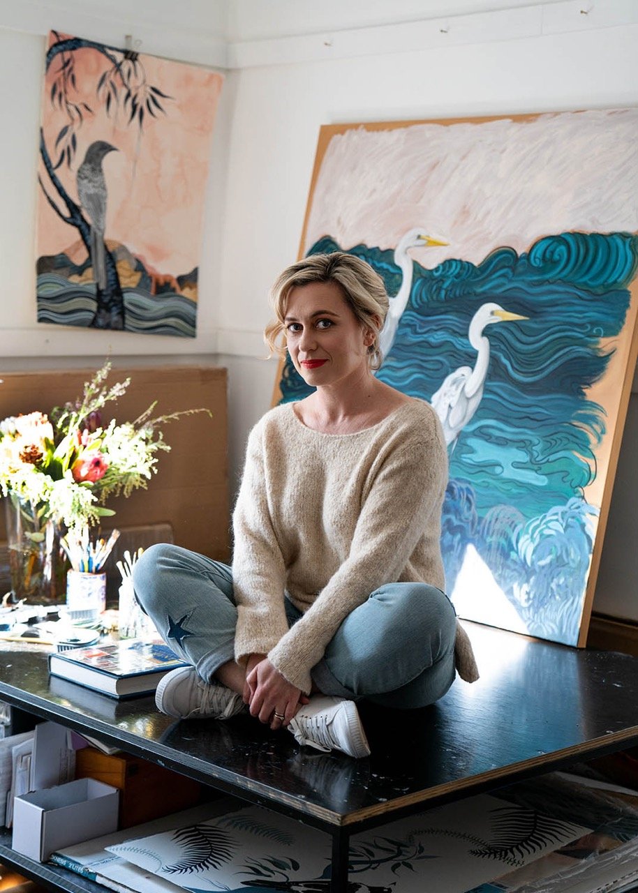 Local Sydney artist Sally Browne sitting atop a table in her studio