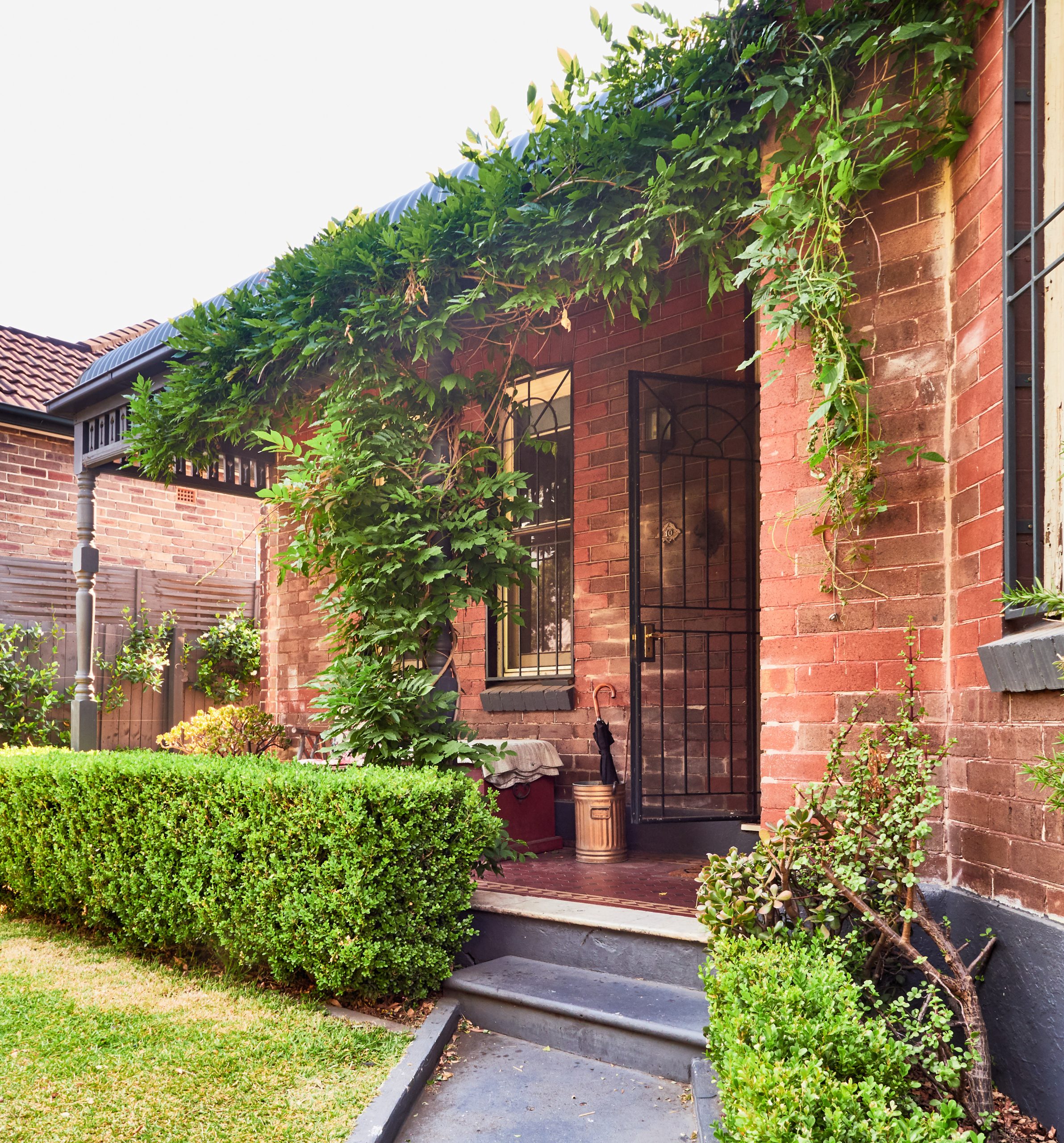 Entrance to red brick home with vines covering the verandah