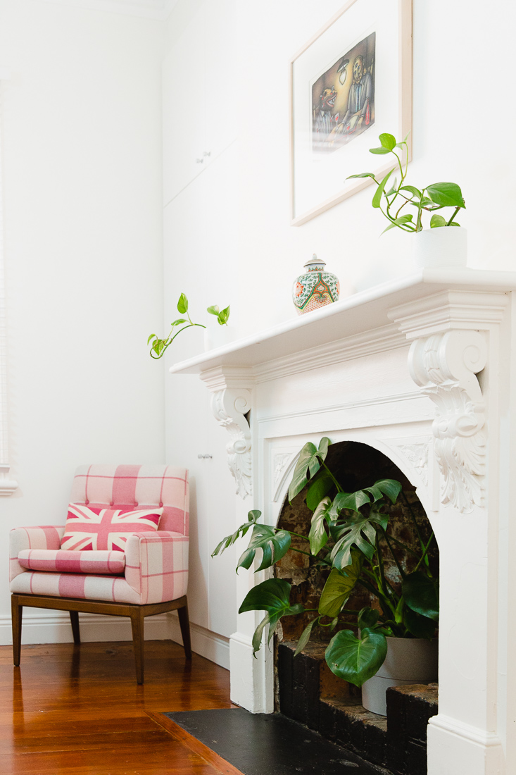 Pink chair, house plants and traditional fireplace painted white
