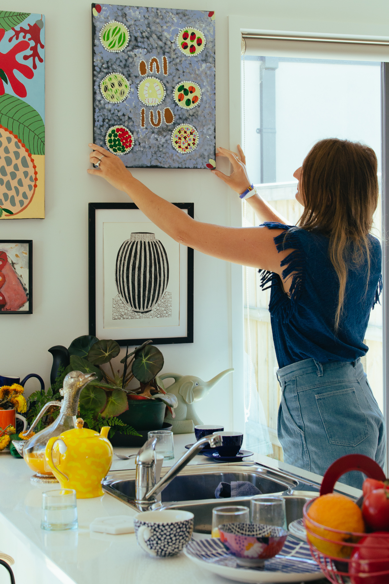 Kate Rogers adjusting the four small artworks above the kitchen counter