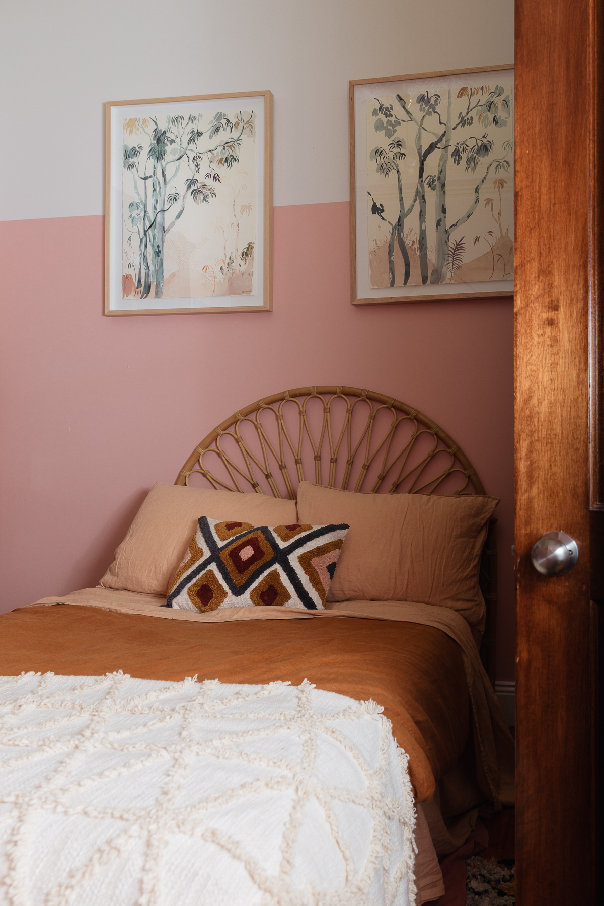 Pink walled room with two watercolour artworks hanging above a rust and terracotta bed