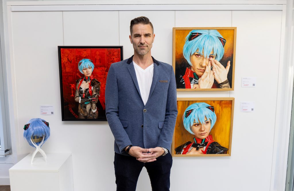 Tom poses with his paintings of Zio_cos, dressed as a character from the Japanese animated series Neon Genesis Evangelion.