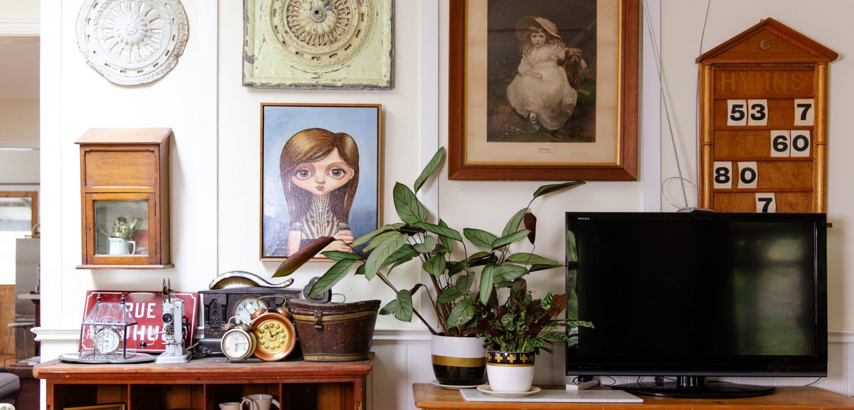 A room in Alicia's home with artwork on the wall and furniture covered with antique items.