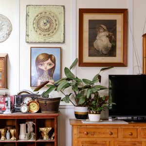 A room in Alicia's home with artwork on the wall and furniture covered with antique items.